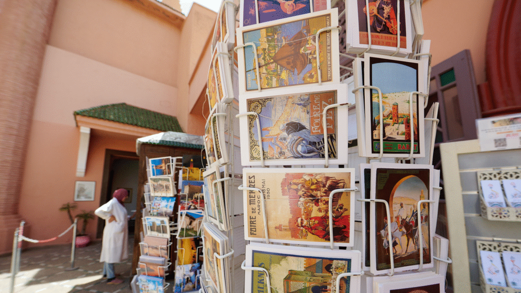 Postcard vendor outside Moroccan Museum of Art in Marrakesh, showcasing local culture and traditional souvenirs at the bazaar entrance.
